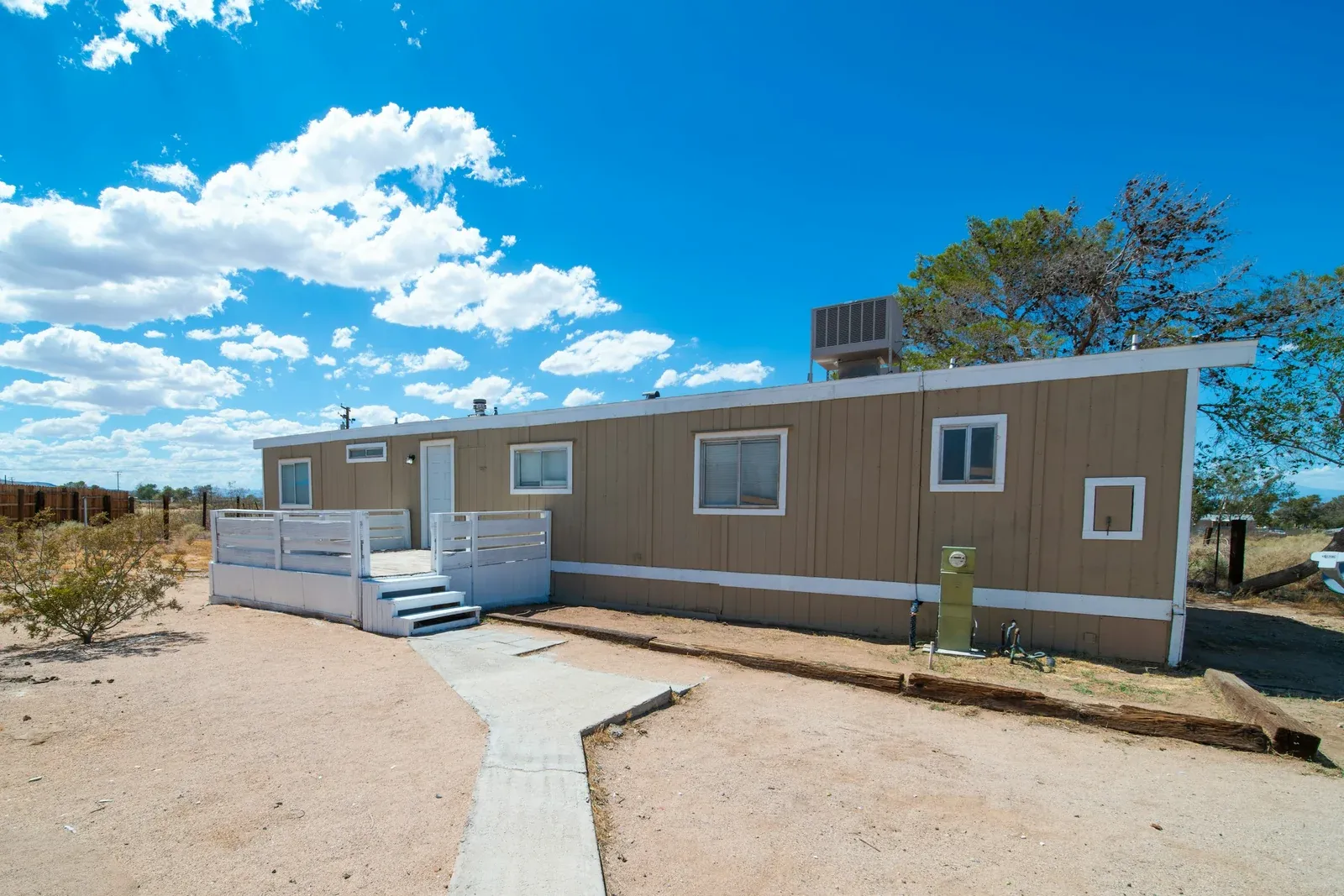 A single-wide manufactured home with tan siding, white trim, and a white deck with front steps